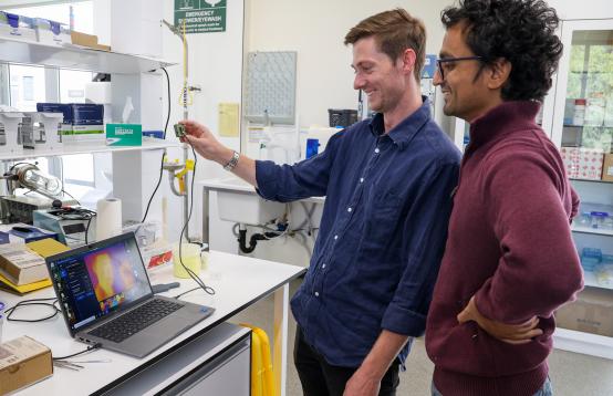Two people standing in front of a laptop in a lab