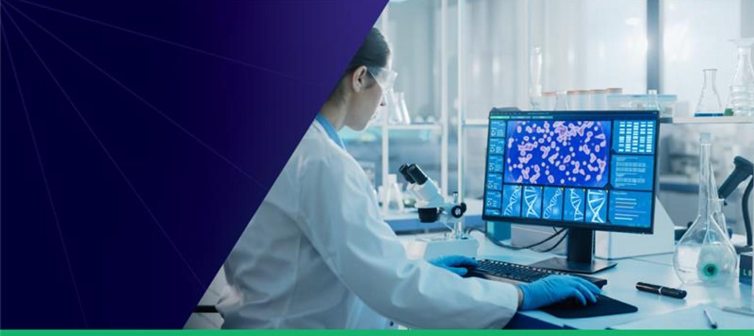 AEA Ignite R3 - Scientist in a white coat wearing safety glasses and working on a computer.